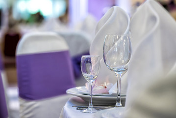 Glasses, forks, knives, napkins and decorative flower on a table served for dinner in cozy restaurant.