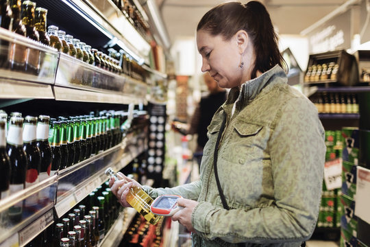 Side view of woman scanning beer bottle in supermarket
