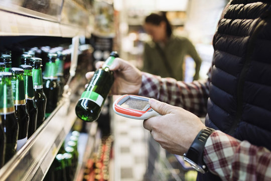 Midsection of male customer scanning beer bottle in supermarket