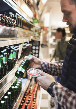 Man scanning beer bottle with barcode reader in supermarket