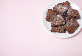 A plate full of freshly baked chocolate fudge brownies on a pastel pink background with empty space at side