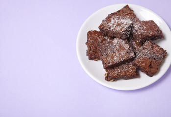 A plate full of freshly baked chocolate fudge brownies on a pastel purple background with empty...