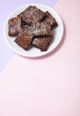 A plate of freshly baked chocolate fudge brownies on a pastel pink and purple background with blank...
