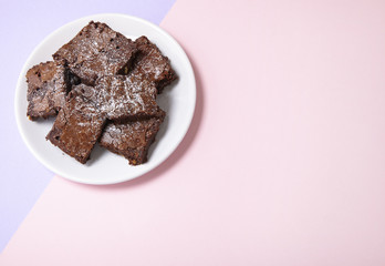 A plate of freshly baked chocolate fudge brownies on a pastel pink and purple background with a blank space at side