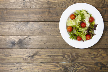 A bowl of fresh garden salad on a rustic wooden dining table background with blank space at side