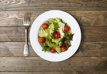 Overhead view of a bowl of fresh garden salad on a rustic wooden dining table background