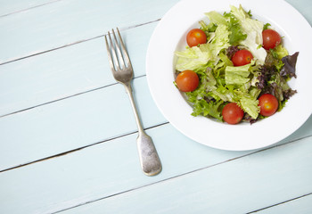 A dish of classic side salad on a blue wooden table background, with fork and blank space at side