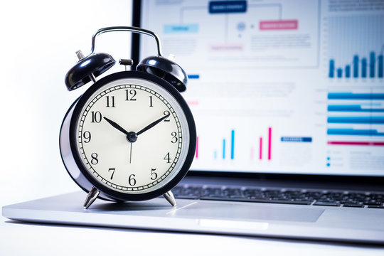Clock alarm with stock graph chart in laptop screen background.