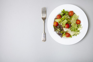 Aerial view of a dish of classic side salad on a pastel grey background with fork and blank space at side