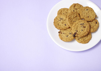 A plate full of freshly baked oatmeal and raisin cookies on a pastel purple background with blank space at side