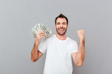 Cheerful excited young man holding dollars and celebrating success