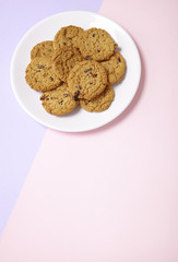A plate full of freshly baked oatmeal and raisin cookies on a pastel pink and purple background with blank space below