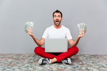 Man sitting on the floor with laptop and holding money