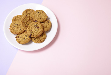 A plate full of freshly baked oatmeal and raisin cookies on a pastel pink and purple background with blank space at side