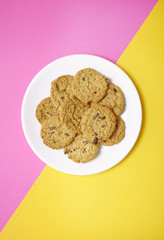 A plate full of freshly baked oatmeal and raisin cookies on a bright pink and yellow background