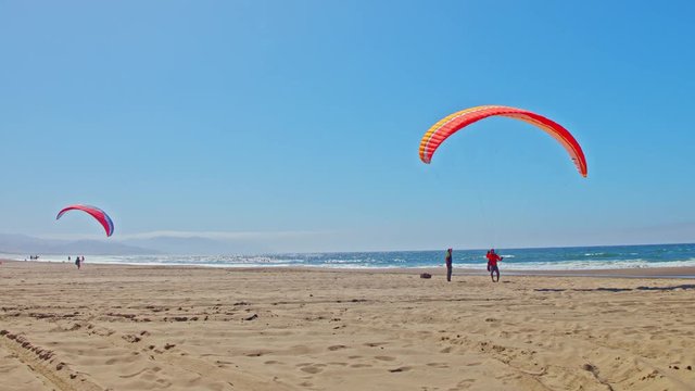 Instructor giving paragliding lesson to a student on a Pacific ocean beach on a sunny day by Cape Kiwanda in Oregon, cinematic, smooth, sliding, panning camera shot