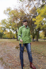 Woman walking with an umbrella in a park with yellow leaves falling from trees