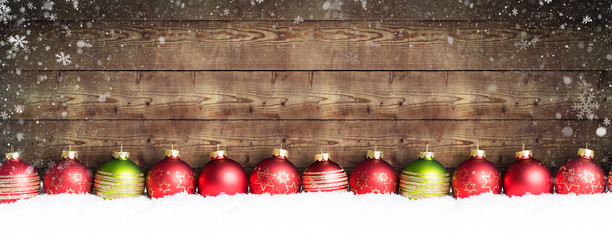 Weihnachtskugeln im Schnee vor einer Holzwand