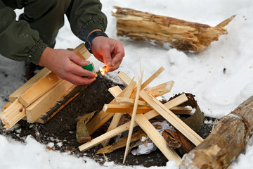 A man strikes a match to make a fire in the winter forest.