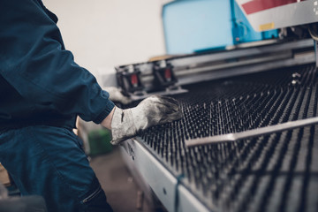 Manual worker doing some steel cutting job in factory for production boiler stoves. Dark conditions. Selective focus. Low light.