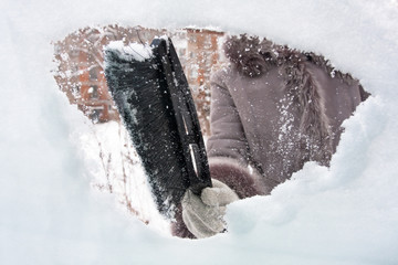 hand cleaning window of car from the snow with brush
