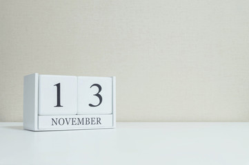 Closeup white wooden calendar with black 13 november word on blurred white wood desk and cream color wallpaper in room textured background with copy space , selective focus at the calendar