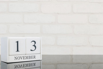 Obraz premium Closeup white wooden calendar with black 13 november word on black glass table and white brick wall textured background with copy space , selective focus at the calendar