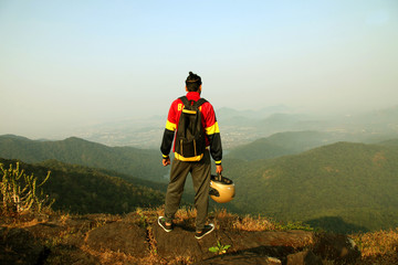 Obraz premium Young man with backpack and helmet standing on the top of a mountain and enjoying valley view