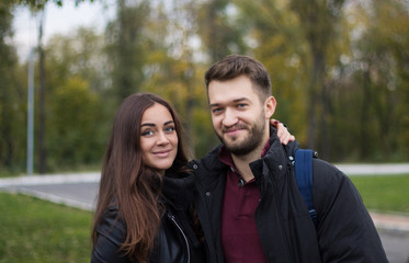 Closeup shot of young beautiful stylish couple in autumn park. She is kissing him. He has a beard. She has a piercing in the nose. She wears black hat with bubo. Natural photo