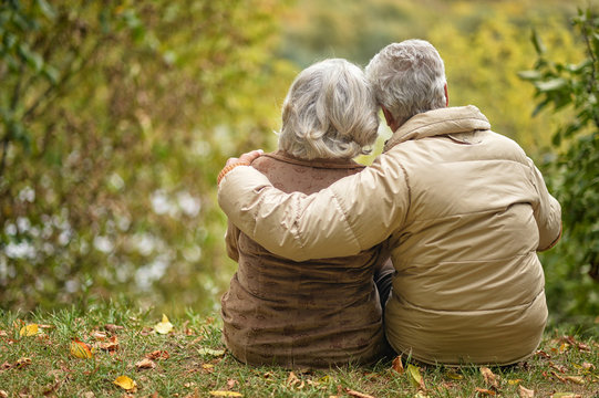 Elderly couple sitting with his back embracing in autumn park