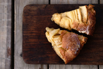 Slice of a french apple cake with vanilla and rum on a cutting board. Wooden background