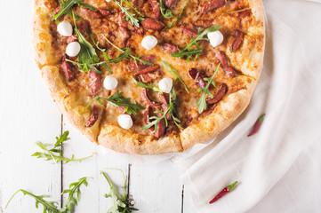 Thick-crust pizza with hunting sausages, mozzarella cheese on a white wooden background