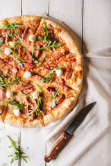 Thick-crust pizza with hunting sausages, mozzarella cheese on a white wooden background