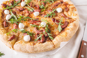 Thick-crust pizza with hunting sausages, mozzarella cheese on a white wooden background
