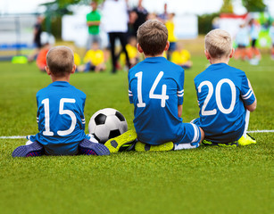 Children In Blue Sportswear Sitting On Soccer Pitch And Watching Football Soccer Match. Kids Soccer Tournament. Youth Soccer Background