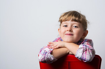 child looks out from behind a leather chair