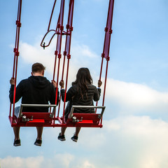People having fun In swing carousel against blue sky.