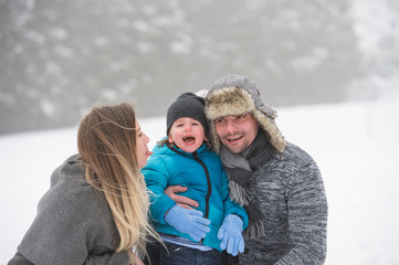 Father and mother with their son, playing in the snow.