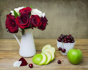 Still life with beautiful bunch of red and white roses placed in white jug,fresh cherries, green apples on rustic wooden table.