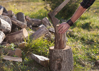Man in jeans and checkered shirt standing near stump with ax in hands