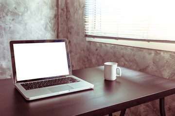 Laptop with white blank screen, white cup of coffee on the desk.