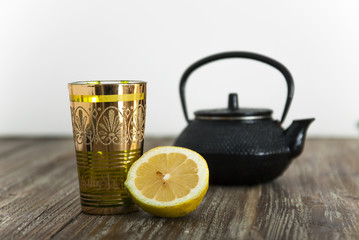 infusión de té, vaso, tetera y limón, sobre mesa de madera