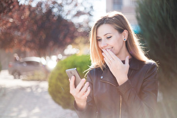 Young smiling woman reading funny message on teletphone. Autumn city background