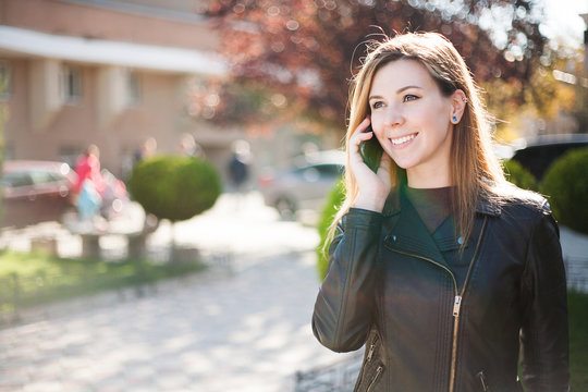 Young smiling woman talking on mobile phone. Autumn city background  