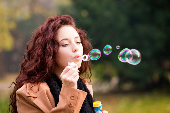young woman having fun and blowing soap bubbles in park