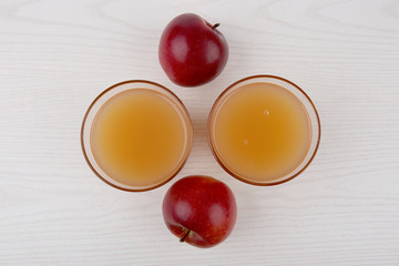 Two red apples and two glasses of juice on white wooden background. Top view.