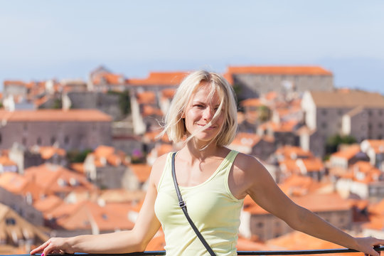 Beautiful young blonde girl on a background of blurred panorama of Dubrovnik old town. Beautiful view of the walled city, Dubrovnik Croatia. The mysterious atmosphere and processing.