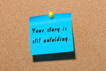 Your Story Is Still Unfolding motivation inscription written on blue sticker pinned at cork notice background