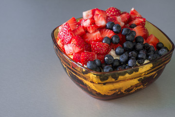 Fresh cottage cheese with cut strawberries and blueberry in yellow glass bowl. Healthy breakfast.