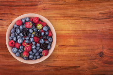 Brown ceramic plate with berries on the left of the wooden table with clipping path. Top view.